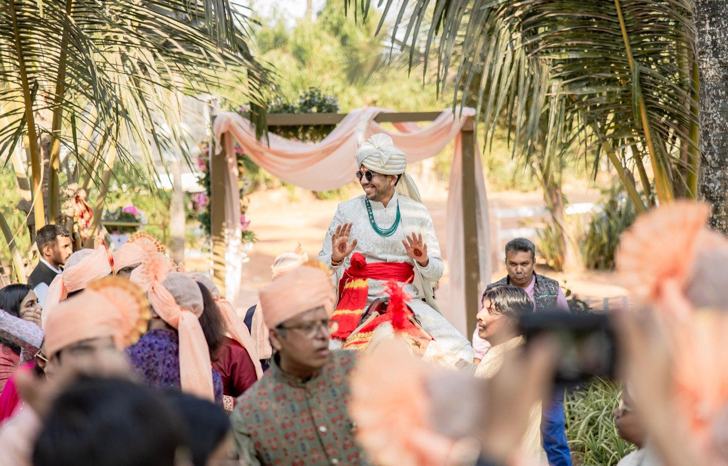 The groom arriving on horseback beneath palm trees for his baraat in Goa