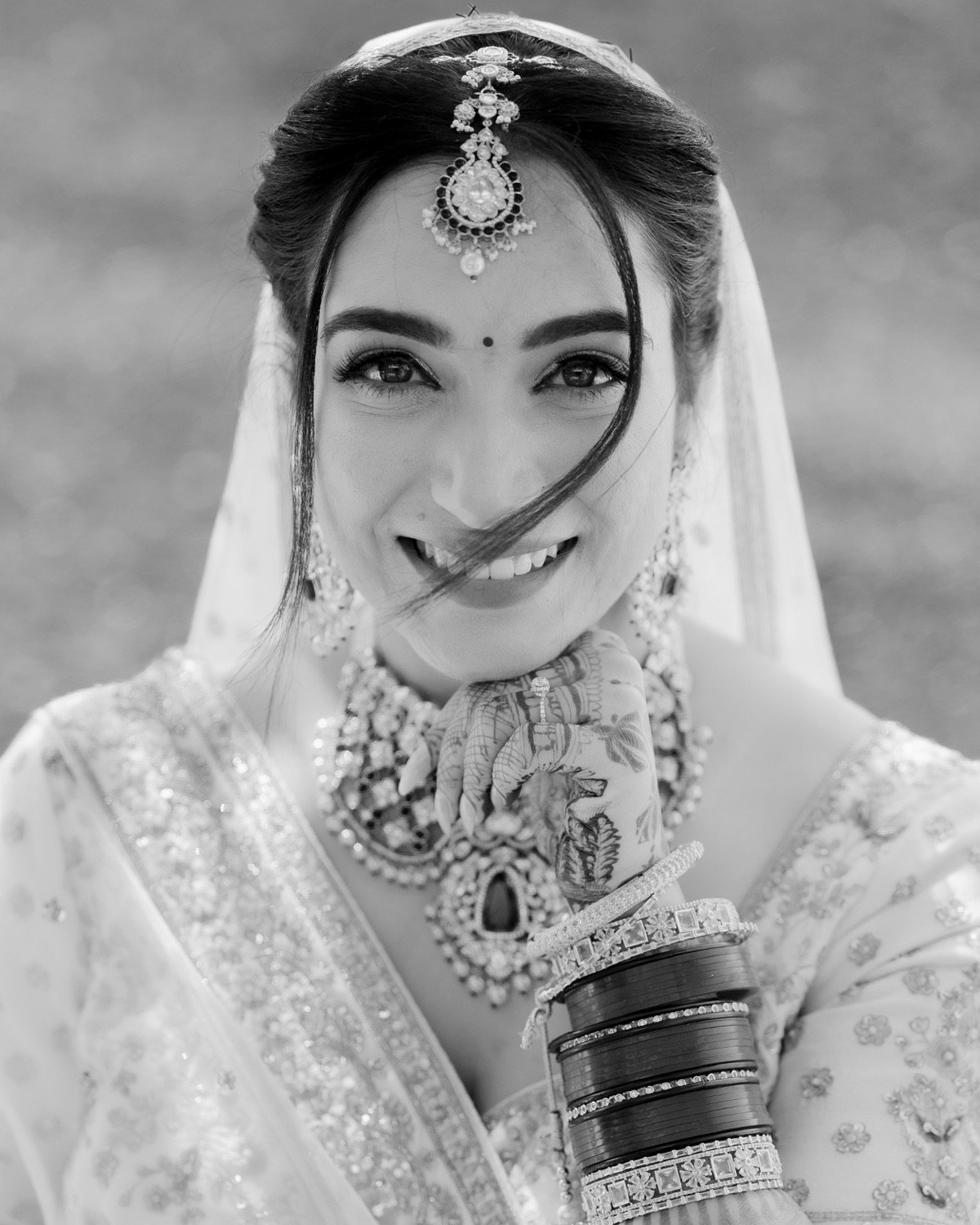 Black and white bridal portrait of Shivani smiling in her veil and maang tikka